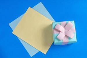 Small gift box with a pink ribbon on a blue background and a blank card for your message. photo