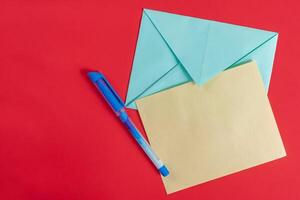 Blue envelope with a blank yellow paper and pen on a vibrant red background. photo