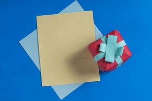 Red gift box with a blue ribbon and papers on a blue background. photo