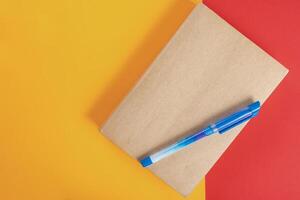 Notebook with pen on top on a bright yellow and red background. photo