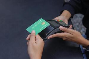 Close up of credit card payment using a point of sale terminal. Close-up of hand swiping a green card while another person waits at a table. Modern cashless transaction concept. photo