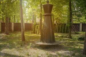 Park bench in the form of a chess piece in the park in the rays of the setting sun. Park with tall trees, green lawn on a sunny day photo