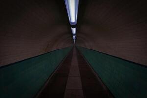 Empty pedestrian tunnel with turquoise tiles and lights illuminating the path photo
