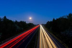 Highway with light trails and full moon at dusk photo