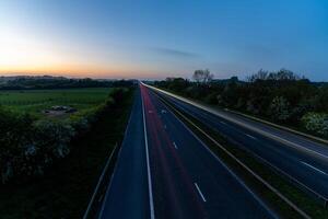 Highway with light trails at dawn illuminating the asphalt near the countryside photo