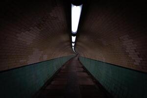 Long illuminated pedestrian tunnel with green tiles and brick walls photo