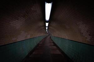 Long, dimly lit tunnel with brick walls and tiled wainscoting photo