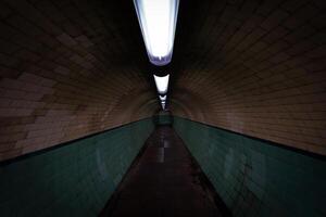 Empty pedestrian tunnel with green tiles and lights illuminating the path photo