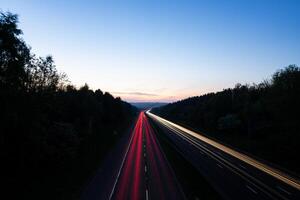 Light trails illuminating highway at dusk between forests photo