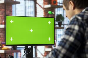 Man in living room office using mockup PC to answer emails from business associates. Close up of remote employee typing on green screen device keyboard, solving tasks in apartment photo