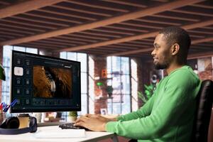 Smiling man using AI program turning text prompt into videos, pleased by results. Joyous african american person interacting with text to artificial intelligence generative model photo
