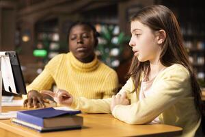 Young diverse students attending an online class via call in the library, focused on distance learning and completing a school assignment using modern digital technology. Webinar work. photo