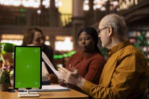 Mature group of college students read next to a green screen device, diverse people working on their thesis citations and documents. Analyzing coursework in a peaceful library. photo