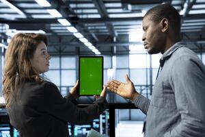 Team of server hub engineers using green screen laptop, conducting security audits. IT specialists in data center reviewing firewall rules on mockup device, logging incident details, talking photo