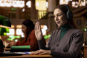 Female student joins a remote call for an online university course, studying digital materials and preparing a college project in a calm study space with books and academic focus. photo