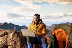 Workaholic explorer always connected and addicted to uninterrupted work, opening his laptop on the mountain top. Young hiker traveler with internet dependency enjoys strong signal. photo