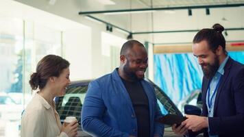 Showroom agent completes paperwork accompanying vehicle sale, shaking hands with clients and offering car keys. Salesperson in dealership signing contract with customers, reaching agreement, camera A photo
