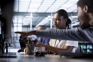 Data center engineer helping colleague, pointing finger to screen, using programming languages to construct algorithms and build applications. Server farm IT expert showing code to coworker on monitor photo