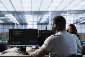 Technician in server farm workspace protecting data threatened by hacking attacks on computers. African american IT professional writing code, safeguarding data center from unauthorized access photo