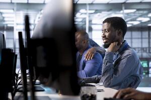 Smiling engineer in data center next to colleagues updating systems to keeps performance up and protect servers from software vulnerabilities. Coworkers looking for errors causing servers to slow down photo
