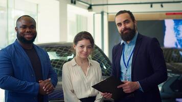Portrait of cheerful salesman talking with customers, showcasing dealership vehicles and explaining their features. Happy showroom agent presenting car characteristics to clients, camera A photo