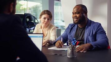 Customers in showroom completing credit application and financing paperwork after deciding to purchase new car. Salesman in dealership discussing financing options with clients, camera B photo