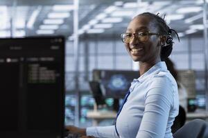 Portrait of cheerful woman tasked with doing checkup on server room rows providing computing resources for different workloads. Joyful admin investigating data center mainframes using PC photo