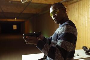 Portrait of man in shooting range doing training, learning firearm safety and proper gun handling. Person practicing with pistol, wearing safety glasses to prevent debris from getting in eyes photo