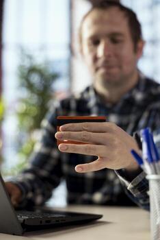 Close up of credit card used by shopper doing online payments during checkout process. Focus on debit card used by person in blurry background using internet marketplace to make purchases photo