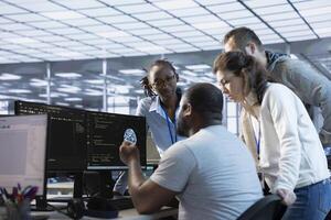 Team of engineers working in server farm, using PCs to analyze data. Multiracial group of employees examining infrastructure in data center, ensuring system integrity and security photo