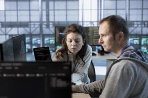 Team leader showing intern how to use machine learning to optimize data center operations. Close up of supervisor talking with employee implementing server virtualization photo