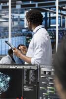 Data center admin uses AI visualization technology on tablet to oversee automated repetitive tasks. Server farm IT professional modifying infrastructure rigs systems based on data analytics graphs photo