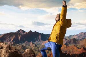 Happy adventurer embraces the thrill of standing at the top of the mountain, feeling the power of accomplishment. Awe inspiring mountain range with peaceful sky and vast wilderness. photo