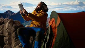 Reckless explorer struggling with wind and weak signal keep internet connection, camping on a scenic rocky mountain peak. Hiker in danger with extreme cold weather, foolish. Camera A. photo