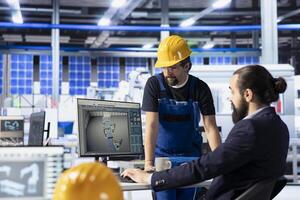 Solar panel plant team leader showing engineer how to adjust robotic machinery settings. Photovoltaics factory manager talking with technician in office, diagnosing gear performance issues photo