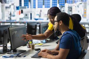 African american engineering team doing quality control on computer setup, troubleshooting and fixing technical issues for solar energy at the factory. Coworkers inspecting system. photo