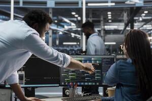 Data center supervisor overseeing admin using PC to visualize artificial intelligence neural networks node trees. Server room manager providing feedback to employee working to oversee AI systems photo