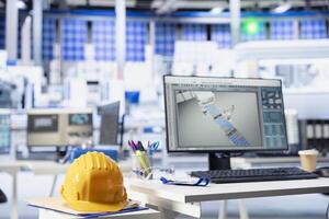 CAD program on PC display in photovoltaics factory used for designing production lines. Simulation software on computer monitor in empty solar panels plant next to yellow hardhat photo
