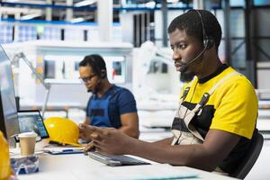 Customer support black technician on helpline in photovoltaic facility answering calls on headset, offering assistance and support in fixing technical issues. Male operator at help desk. photo