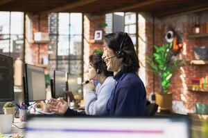 Call center agent laughing while talking with funny customer using headset mic while providing guidance. Customer center employee amused by comical client while providing technical solutions photo