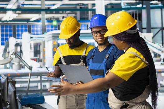 All black team of engineers comparing solar panels designs on laptop, working on the production line at the manufacturing plant. Troubleshooting and debugging to ensure optimization. photo