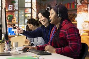 Happy customer service senior manager teaching new employee how to track support tickets in company software. Cheerful Asian call center supervisor shows intern how to create and close support tickets photo