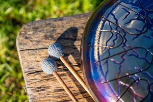 Steel tongue drum and mallets resting on a wooden bench. Concept of sacred stillness, sound meditation, and harmony with nature. High quality photo
