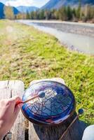 Point of view of person playing a steel tongue drum with mallets in front of mountains and river. Concept of immersive music, self-expression, and unity with natural rhythm. High quality photo
