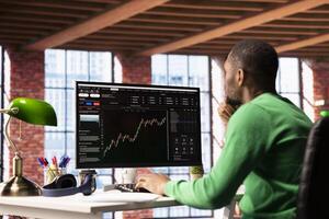 Man using PC to purchase and sell stocks, looking at charts to learn how to maximize profits. African american investor looking at stock exchange graphs on computer monitor photo