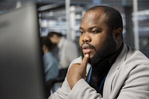 Man working in data center analyzing software logs metrics on PC, optimizing storage systems. African american server farm IT expert inspecting resource utilization, managing application efficiency photo