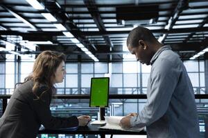 Woman overseeing server room with mockup device, reading documentation paperwork, troubleshooting hardware. Supervisor doing inspection in server hub, reading technical files on green screen tablet photo