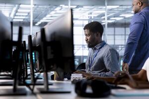 Engineer next to coworkers in server farm checking recovery plan, monitoring data center energy consumption. Employee and colleagues in server room doing routine disk checks photo