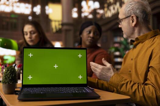 Multiethnic group of people studying together at library next to mockup display, engaged with academic text and paperwork. Working on their degree in a serene public library environment. photo