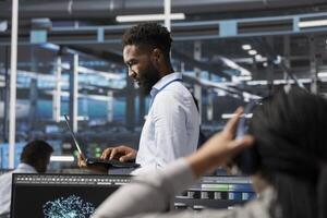 Data center specialist using AI deep learning algorithms on laptop to analyze large datasets. Man in server farm using artificial intelligence on notebook to recognize patterns in facility data photo
